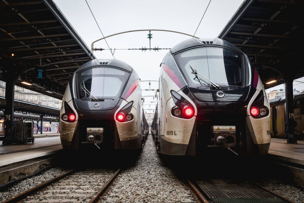 Two modern electric trains on parallel tracks at a station, facing the camera with overhead wires above them.