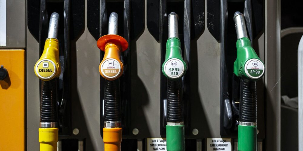 Four fuel nozzles at a gas pump from left to right: yellow B7 Diesel, orange B7 Excellum Diesel, green SP95 E10, and green SP98 Excellium with lever handles