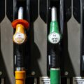 Four fuel nozzles at a gas pump from left to right: yellow B7 Diesel, orange B7 Excellum Diesel, green SP95 E10, and green SP98 Excellium with lever handles