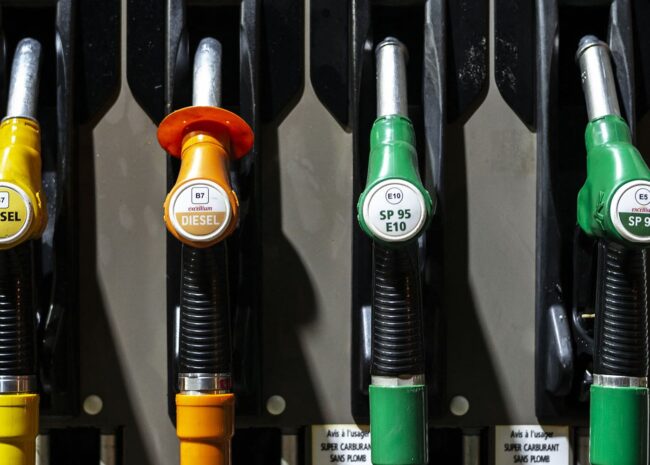 Four fuel nozzles at a gas pump from left to right: yellow B7 Diesel, orange B7 Excellum Diesel, green SP95 E10, and green SP98 Excellium with lever handles