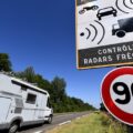 A white motorhome parked on the roadside with a large 90 km/h speed limit sign and a radar control sign in a rural area under a clear blue sky.