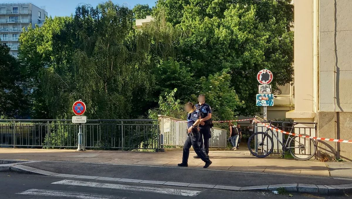 Two police officers walk along a sidewalk near a bike chained to a railing and red-and-white tape, with green trees in the background.