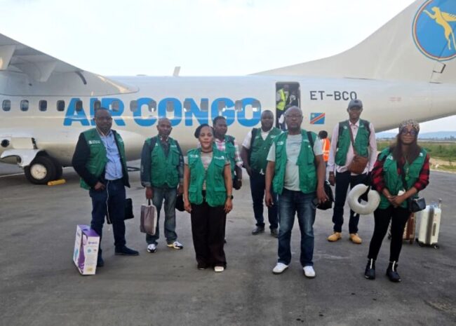 Group of airline staff in green vests posing on the tarmac in front of a blue-and-white Air Congo airplane, tail logo visible.