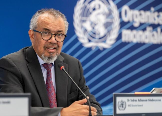 Man in a suit and glasses speaks into a microphone at a United Nations press briefing, with the UN emblem in the blue background.