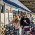 People with bicycles and helmets gather at a platform beside a white SNCF train with a Région Normandie emblem, smiling and ready to board.