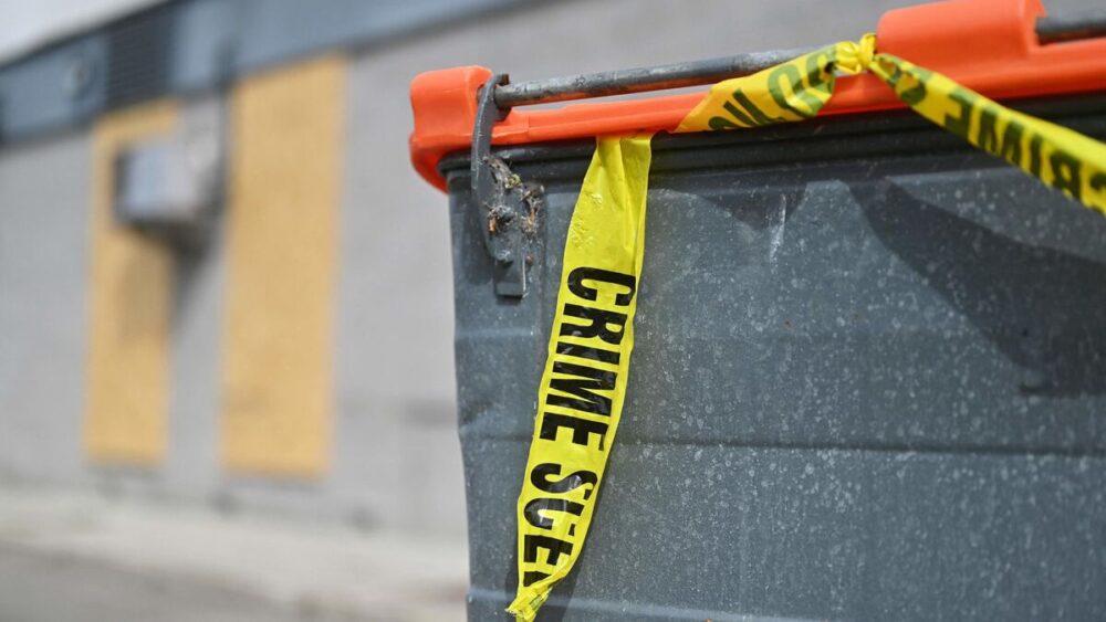 Rotherham residents talk about immigration concerns 10 days after far right riots - MultiPol 360 Grey dumpster with bright yellow crime scene tape draped across the top, in an industrial area.