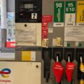 Gas pump at a TotalEnergies station with multiple fuel options (98, 95 E10, diesel) and red 'hors service' hose covers; urban street in background.