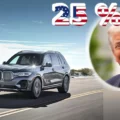 Silver SUV driving on a coastal highway with a patriotic '25%' graphic and a circular portrait of a smiling man in a suit on the right.