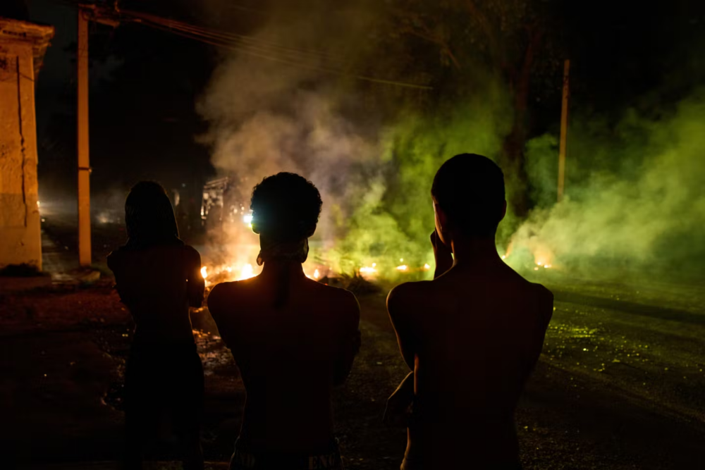 image_2026-05-19_00-12-03 - MultiPol 360 Three silhouetted figures with bare backs stand on a dark street at night, facing glowing embers and colored smoke.
