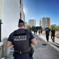 Back view of a police officer in tactical vest on an urban street with a group of officers in the distance