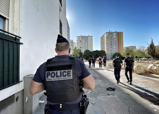 Back view of a police officer in tactical vest on an urban street with a group of officers in the distance
