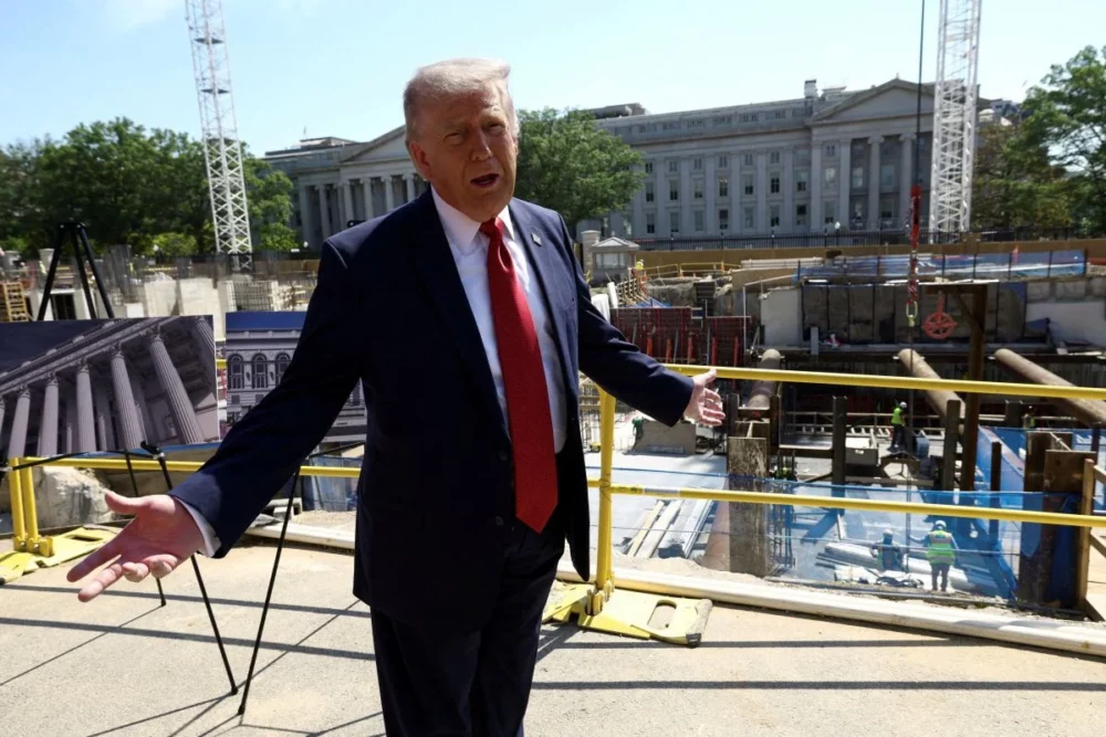 Trump_25 - MultiPol 360 Politician in a dark suit and red tie speaks with arms outstretched on a construction site, with a large government-style building in the background and construction equipment around.