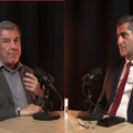 Two men sit at a round table with microphones, appearing to host a podcast or interview in a studio.
